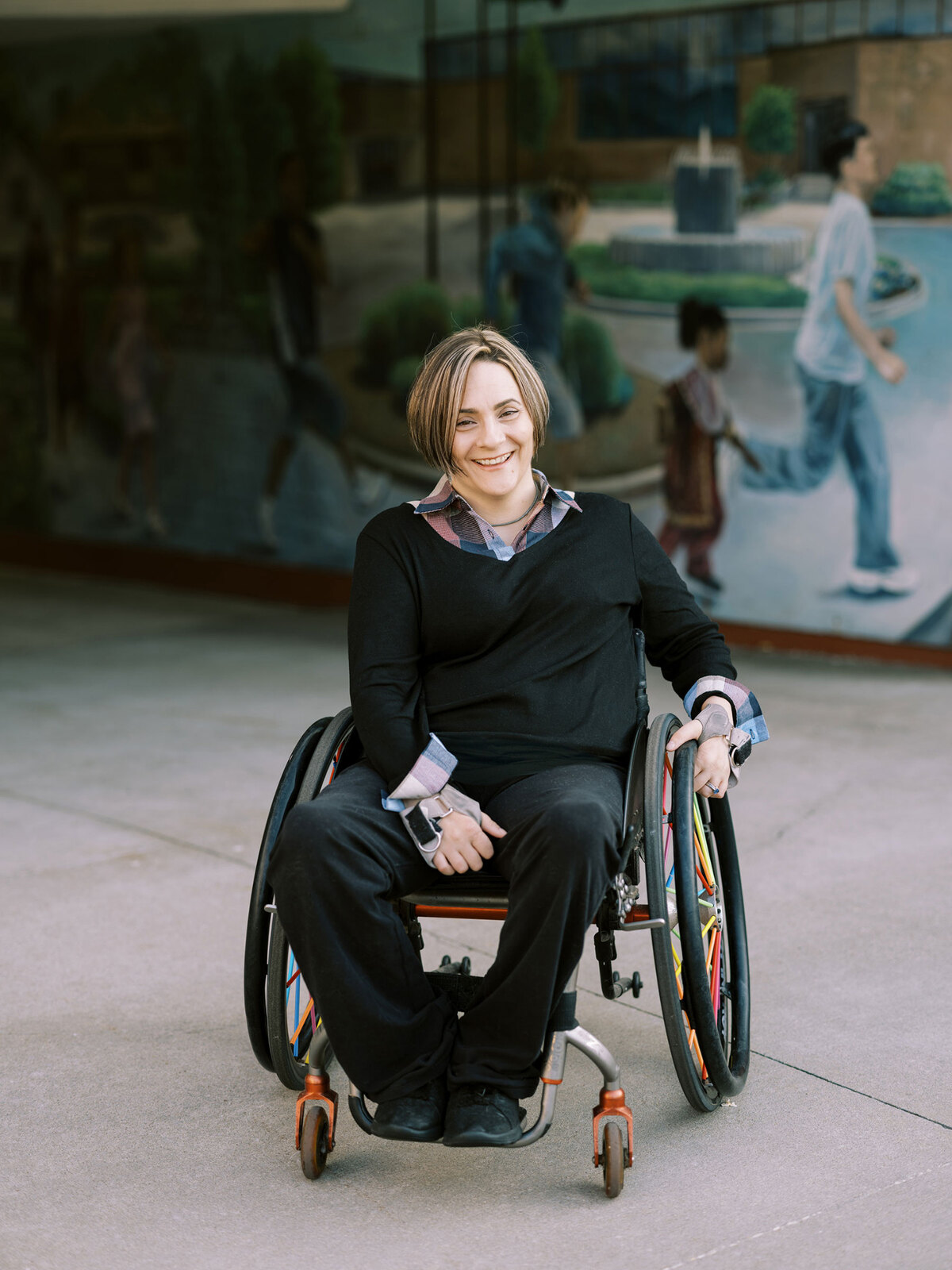 Allaina Humphreys smiling in her manual wheelchair outside a glass-fronted building