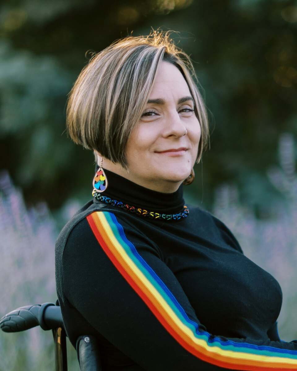 Allaina Humphreys smiling outdoors in her wheelchair, wearing a black top with a rainbow stripe on the sleeve