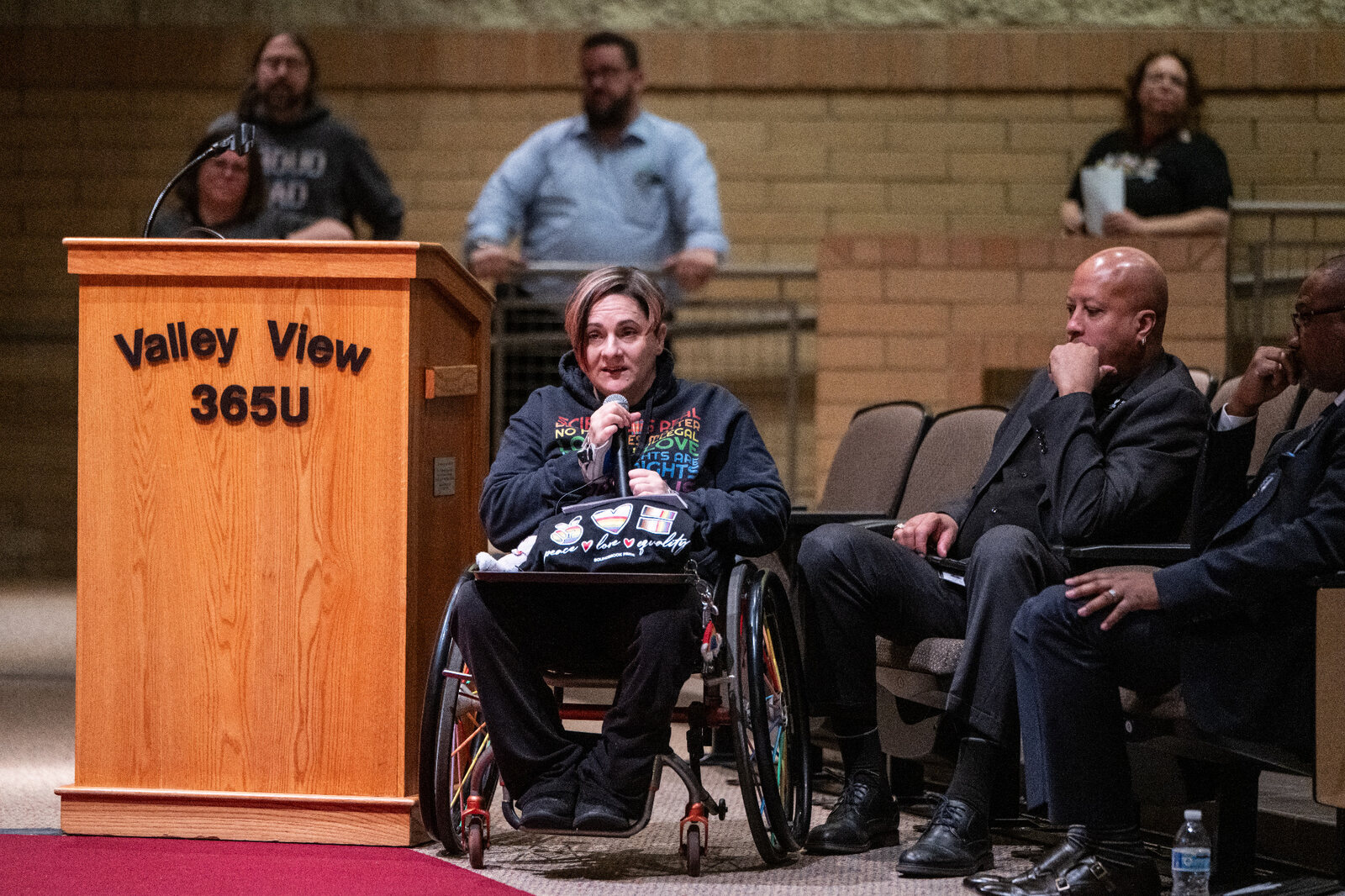 Allaina speaking from her wheelchair beside a podium during a community gathering
