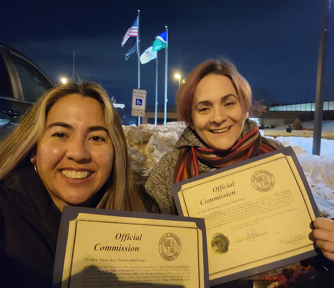Allaina and artist Mithra holding official commission certificates outdoors at night